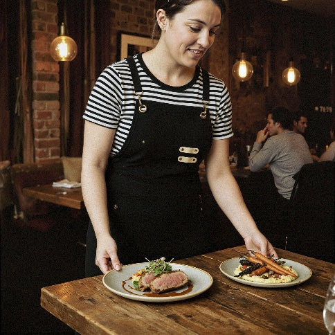 Server carrying plates wearing The Wine Chic cross-back apron